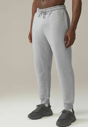 Pantalones de chándal grises hechos de una tela suave, con cinturilla elástica y cordón. Ajuste cónico con puños acanalados en los tobillos.