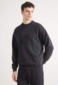 Czarna bluza z okrągłym dekoltem i haftowanym logo "HUGO". Posiada ściągacze na rękawach i dole, a także teksturalne wykończenia. Miękki materiał.