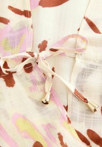 Lichtgewicht, crème-kleurige stof met roze en bruine abstracte patronen. Beschikt over een striksluiting met gouden metalen accenten en een zachte textuur.