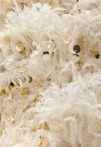 Țesătură albă texturată care prezintă fibre desfăcute și paiete aurii dispersate, creând un aspect stratificat, moale, cu detalii reflective.