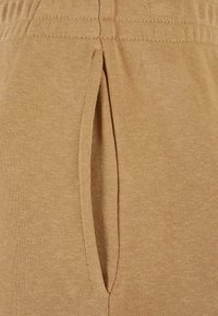 Beige, schmal zulaufende Hose aus einem weichen, dehnbaren Stoff, mit Seitentaschenöffnung und einem elastischen Bund für Komfort und passgenauen Sitz.