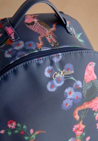 Jūrinės spalvos audinys krepšys su gėlių ir paukščių motyvais. Aukso spalvos prekės ženklo „Cath Kidston“ logotipas ant užtrauktuko, tekstūruotas paviršius su blizgiu apdaila.