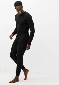 Čierny dlhý rukáv a priliehavé nohavice, vyrobené z mäkkej tkaniny. Má okrúhly výstrih a rebrované manžety. Nosené bosými nohami na svetlom povrchu.