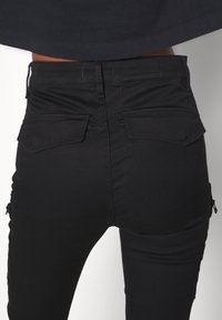 Černé džíny s vysokým pasem, zadními kapsami, hladkou texturou a bočními zipy na nohavicích, s úzkým střihem.