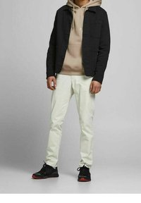 Chaqueta negra, sudadera beige, pantalones de color claro y zapatillas negras con acentos rojos. Texturas de tela suaves; diseño casual en capas.