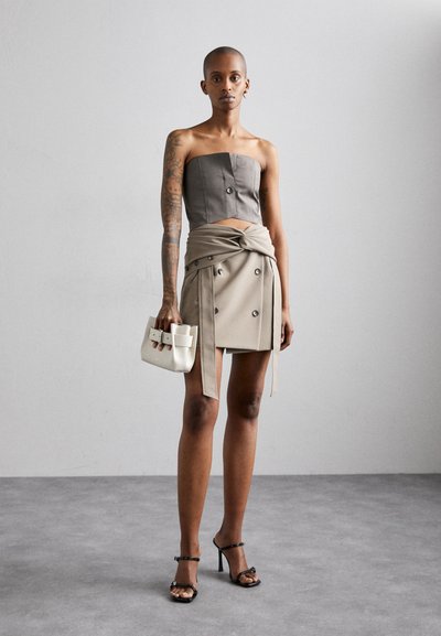 Strapless gray top with front buttons, paired with a beige wrap skirt featuring buttons. Model holds a small white bag and wears black heels.