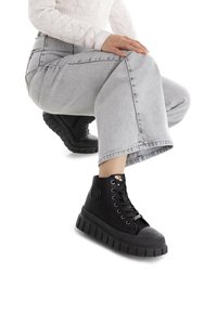 Zapatillas altas negras con una suela de goma gruesa, punta redonda y cierre con cordones. Presenta un logo en el lateral y un material superior texturizado.