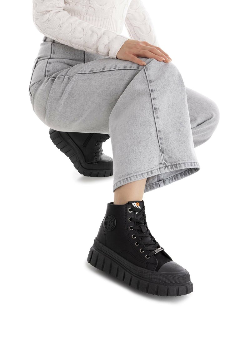 Zapatillas altas negras con una suela de goma gruesa, punta redonda y cierre con cordones. Presenta un logo en el lateral y un material superior texturizado.