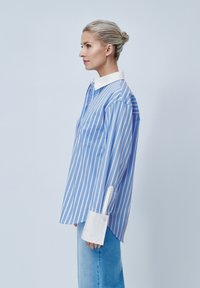 Ριγέ μπλε και λευκή μακρυμάνικη μπλούζα με φαρδύ γιακά, τσέπη και λευκές λεπτομέρειες στους καρπούς. Μαλακό ύφασμα, χαλαρή εφαρμογή και casual σχέδιο.