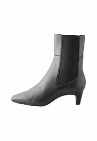 Bottine en cuir noir avec un bout pointu, des panneaux latéraux élastiques et un talon bas. Texture lisse avec des détails de couture minimalistes.