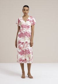 Robes midi fleuries avec des manches courtes et flottantes, présentant un devant boutonné. Les couleurs incluent le rose, la crème et le vert clair dans un motif aquarelle.