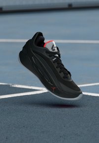 Μαύρο αθλητικό παπούτσι με επάνω μέρος από δίχτυ, κόκκινες και γκρι λεπτομέρειες, και λάστιχο σόλα. Διαθέτει ορατό λογότυπο και σχέδιο με κορδόνια.