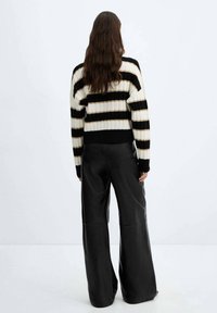 Schwarzer und cremfarbener gestreifter Pullover mit geripptem Stoff, mit breiten Ärmeln und einem cropped Schnitt, kombiniert mit hochgeschnittenen schwarzen Lederhosen.