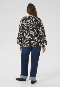 Blouse à motifs noir et crème avec manches bouffantes, associée à un jean bleu avec revers et des ballerines noires. Tissu doux avec une coupe décontractée.