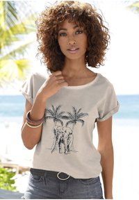 Chemise beige à manches courtes avec un graphisme d'éléphant et de palmiers. Portée avec un short en denim foncé et une ceinture tressée.