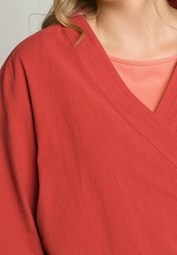 Rotes, geschichtetes Wickeloberteil mit V-Ausschnitt, aus weichem Stoff. Verfügt über sichtbare Nähte entlang des Halsausschnitts und eine pfirsichfarbene innere Lage.