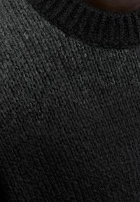 Nahaufnahme von dunkelgrauem und schwarzem gestricktem Wollstoff mit sichtbarem strukturiertem Muster und weichen Fasern.