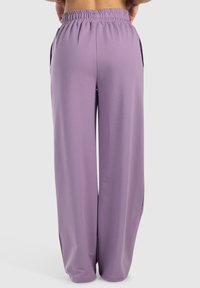 Lila, weite Beinkleider aus leichtem, weichem Stoff mit einem elastischen Bund und seitlichen Taschen, die eine glatte, untexturierte Oberfläche aufweisen.