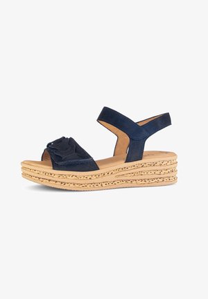 Navy blue suede sandal with ruffled toe design, open back, and two straps. Features a layered cork wedge sole for added height.