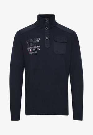 Mørkeblå strikpullover med høj krave, trykknapper, skulderdetaljer og en brystlomme. Har broderet tekst nær lommen.