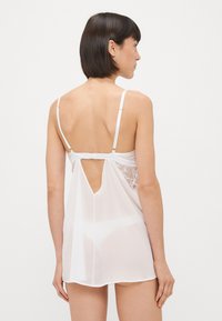 Rochie de noapte albă din material transparent, cu accente din dantelă, bretele ajustabile și un design cu deschidere în spate. Textură fină, croială lejeră și lungime până la genunchi.