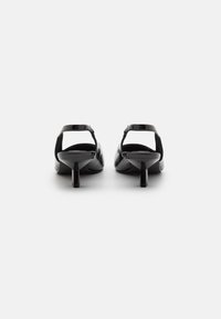 Escarpins en cuir verni noir avec un petit talon carré, un design à dos ouvert et une finition lisse et brillante. Présentent une courbure subtile et une bride à la cheville.