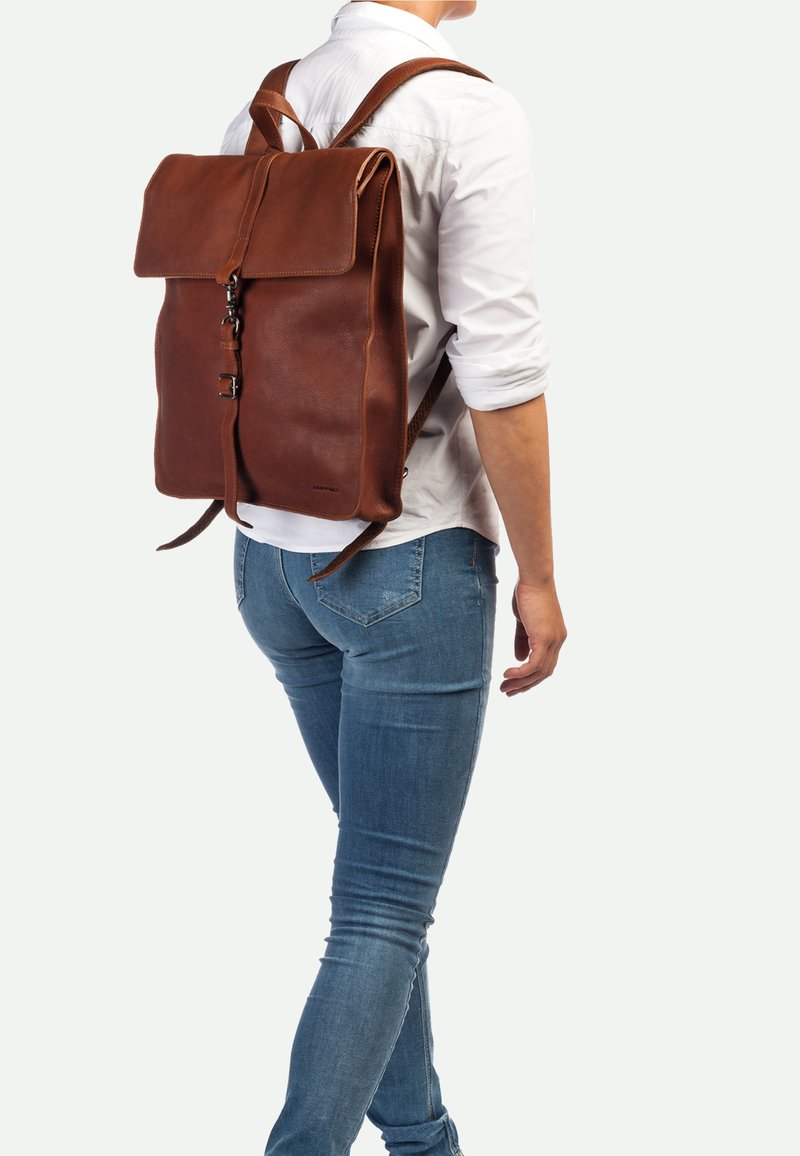 Bruine leren rugzak met een klep sluiting en verstelbare banden, voorzien van een gestructureerd oppervlak en metalen hardware.