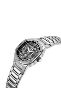 Reloj de acero inoxidable plateado con una esfera esqueletada negra, que presenta subesferas de cronógrafo, una caja redondeada y una pulsera enlazada.