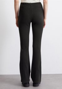 Tummanvihreät, uritetut levenevät housut, joissa on joustava vyötärönauha ja sileä pinta. Helmasta on hieman leveämpi, paljastaen mustat jalkineet.