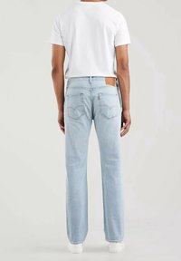 Jeans de denim azul claro con corte recto, que presentan un parche de cuero marrón, dos bolsillos traseros y un detalle de Costura mínima.
