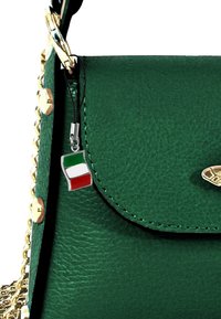 Groene leren handtas met een geprofileerde afwerking, gouden hardware en een metalen charm met de Italiaanse vlag dat aan de hengsel hangt.