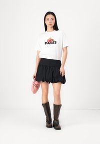 Fehér pamut póló "PARIS" felirattal és virágmintával, melyet egy fekete réteges szoknyával, barna térd fölé érő csizmával és rózsaszín táskával párosítottak.
