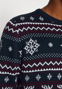 Marinblått stickat tröja med vita och röda Fair Isle-mönster, inklusive snöflingor och zigzag-design, med rundad hals och strukturerad tyg.