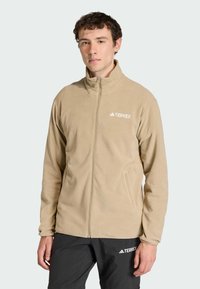 Beige fleec Jacket met een hoge kraag en een rits aan de voorkant. Voorzien van een logo op de borst en zijzakken, ontworpen voor buitenshuis gebruik.