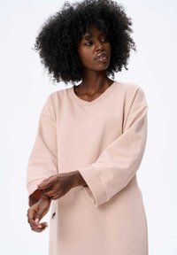 Helles rosa Sweatshirt mit V-Ausschnitt, oversized Passform und überschnittenen Schultern. Verfügt über lange Ärmel und ein strukturiertes diagonales Nahtdetail.
