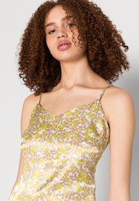 Top de alças florido com acabamento brilhante e semelhante ao cetim em cores pastel, com decote em V e alças finas, adornado com pequenas flores amarelas e cor-de-rosa.