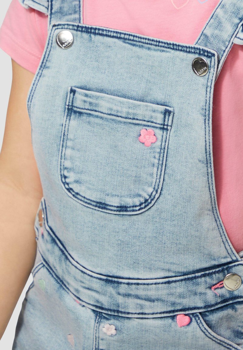Lichtblauwe denim overal met een voorzak en kleurrijke geborduurde accenten, waaronder een roze bloem en hartvormen.