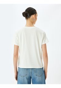 Valkoinen puuvillapaita lyhyillä hihoilla, jossa on pyöreä kaula-aukko. Yhdistetty sinisiin farkkuihin, jotka ovat rentoa istuvuutta ja yksinkertaista muotoilua.