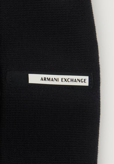 Черна плетена материя с бял правоъгълен етикет с текст "ARMANI EXCHANGE" в черни главни букви.