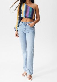 Top multicolore, corto, con spallina unica in un tessuto testurizzato. Abbinato a jeans azzurri a vita alta e sandali bianchi.