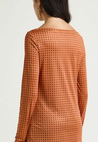 Vestito a maniche lunghe in tessuto arancione con pois viola, caratterizzato da una scollatura ampia e una texture liscia.