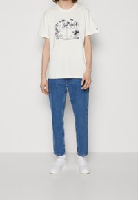 Vit bomulls-t-shirt med marinblått grafiskt motiv som visar blommor och text. Kombinerad med blå denimjeans och vita sneakers.