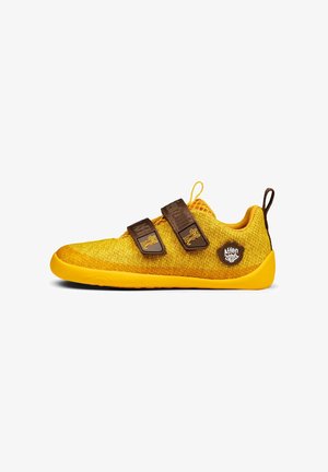 Żółty dziecięcy sneaker z dwoma brązowymi paskami na rzepy i pętelką, dzianą cholewką i gumową podeszwą.