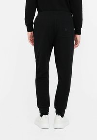 Sorte sweatpants lavet af blødt stof. Har tætsiddende ben, en elastisk talje og en baglomme med en lille etikette.