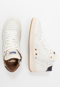 Høje sneakers i hvid læder med perforerede detaljer, en gummisål, guldfarvede hardware-accenter og et lille sort panel ved hælen.