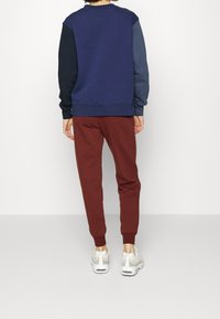Mörkblå sweatshirt med mörkgrå och mörkblå ärmar, kombinerad med röda joggers. Har ribbade muddar och nederkant samt en avslappnad passform.