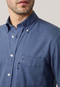 Camisa de manga corta, abotonada, en tela azul oscura. Presenta un bolsillo en el pecho, botones blancos y un acabado sutilmente texturizado.