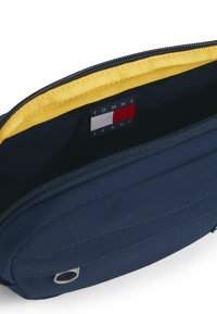 Ναυτικό μπλε θήκη με φερμουάρ, με κίτρινη εσωτερική επένδυση και μικρό λογότυπο Tommy Jeans στο εσωτερικό κοντά στο φερμουάρ.
