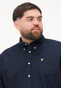 Navy button-up shirt made of cotton, featuring a pointed collar, white buttons, and a small yellow bird logo on the chest pocket.