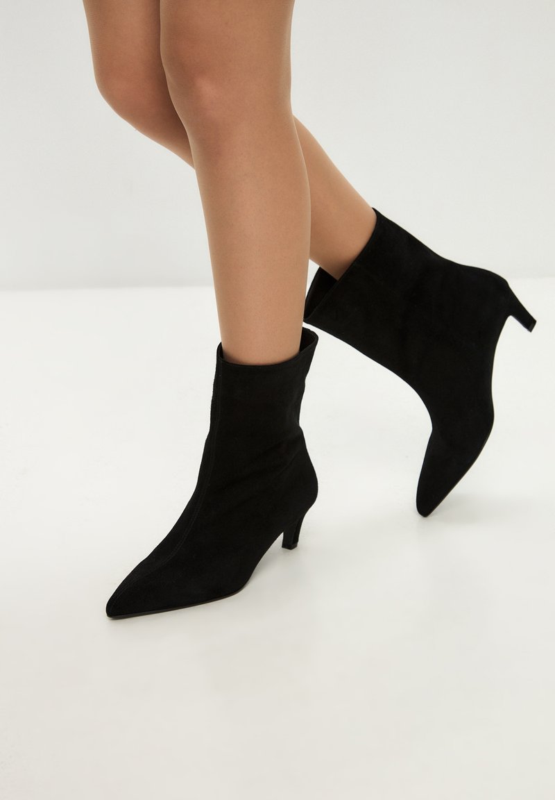 Svarta mockaankelboots med spetsig tå och medelhög klack, med en elegant design och en slät yta, lämpliga för formell klädsel.